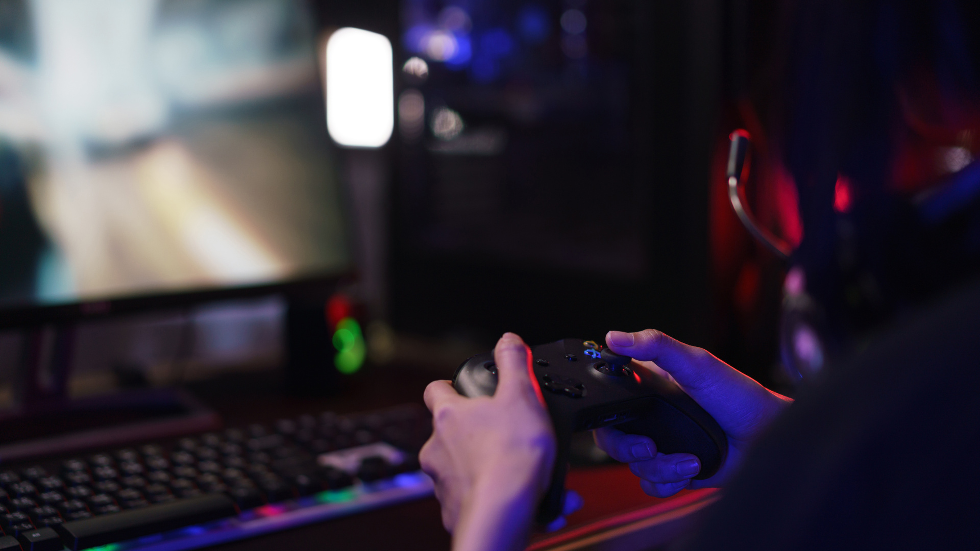 En person håller i en handkontroll för datorspel framför en datorskärm
