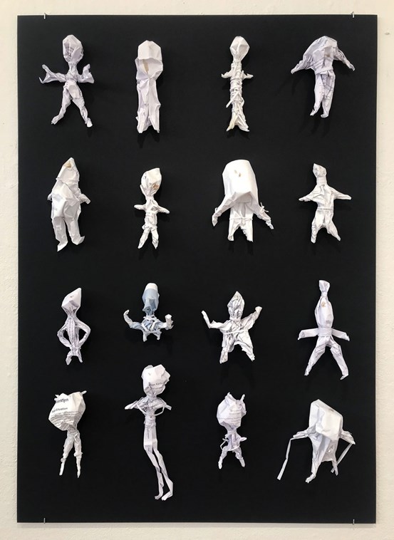 Fyra rader med fyra små vita pappersfigurer i varje rad sitter på en svart tavla, försedda med spår av blod.