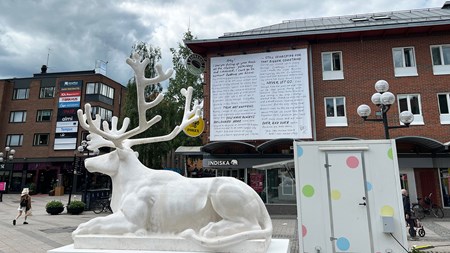 En vit skulptur i stadsmiljö som föreställer ett liggande djur med lejonkropp och renhuvud.
