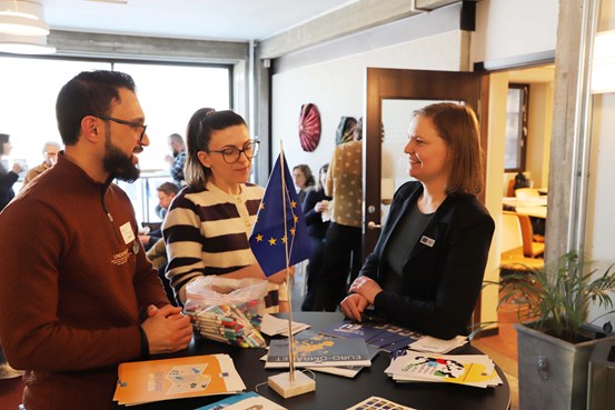 Deltagare på invigningen av Europa Direkt i Härnösand står vid ett ståbord och konverserar. En EU-flagga syns i bilden.