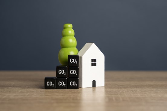 En bild av ett modellhus med en grön pelare bakom och små kuber med texten Co2 som står bredvid. 