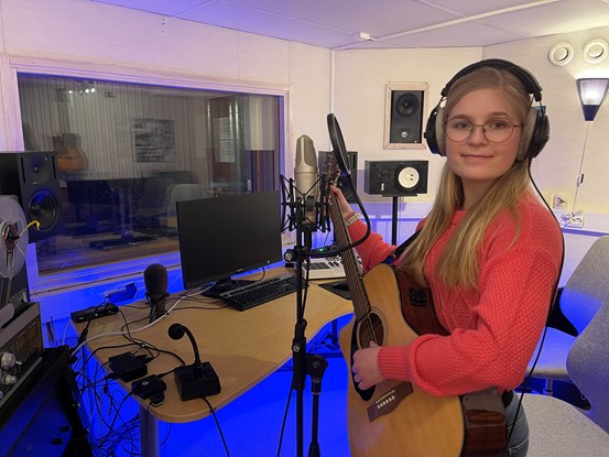 Tjej i röd tröja spelar gitarr i en musikstudio.