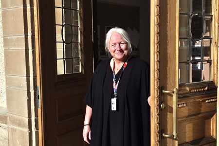 Eva-Lena Norgren står svartklädd i dörröppningen mellan de två tunga entrédörrarna till Örnsköldsviks folkhögskola.