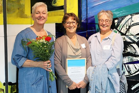 Ingela, Marie och Lillemor från den mobila tandvårdskliniken står uppradade med blommor och diplom. 