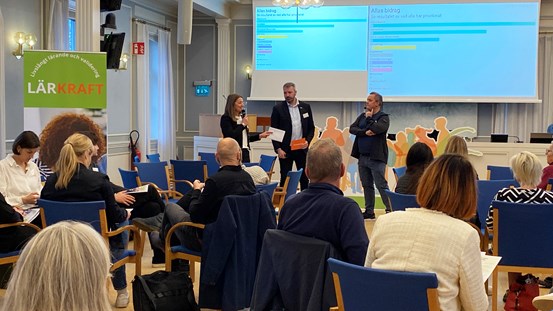 Samling människor som lyssnar till talare framme vid podiet.