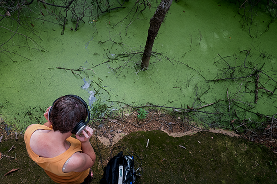 Person med hörlurar sedd uppifrån framför ett gröntonat vattendrag.