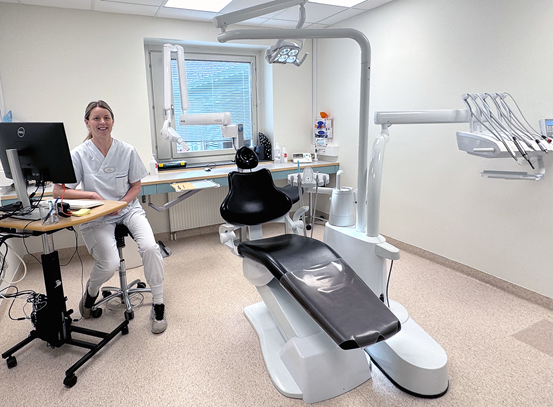 En tandhygienist sitter vid en dator i ett nytt fräscht nyrenoverat undersökningsrum.