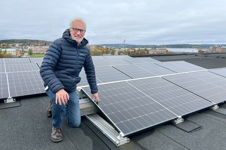 Jan Lindberg står på huk bredvid solcellspaneler som finns på taket av Regionens Hus i Härnösand