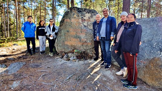 Deltagare från utbildningen står tillsammans med en guide kring en stor sten på ett berg, häxberget