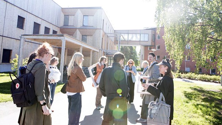 Grupp människor utomhus vid byggnader i High Coast Innovation Park, några med ryggsäckar och anteckningsmaterial, under en guidad aktivitet.