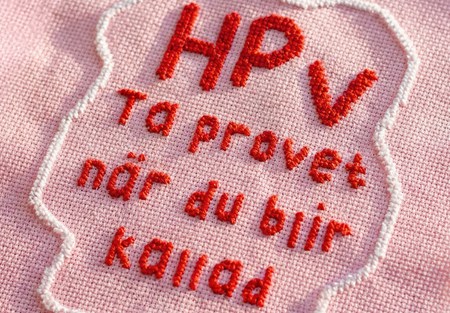 Broderi med röd text på rosa botten med texten HPV Ta provet när du blir kallad.