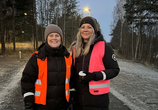 Sara Nylund och Jeanette Hedlund står utomhus i orangea västar vid en gång- och cykelväg.