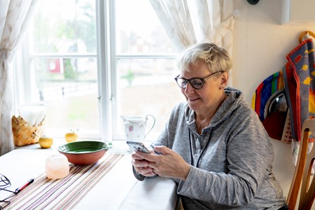 Dam som bokar vaccinationstid via mobilen sittande i sitt kök