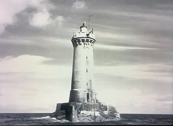 Ett svart-vitt foto från 1923 föreställande en fyr på en liten klippa omgiven av vatten. 