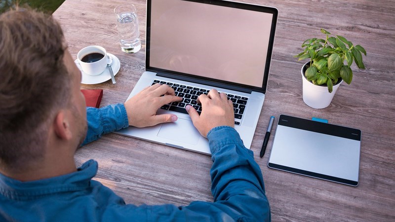 Person arbetar vid laptop med mobil och surfplatta på skrivbord.