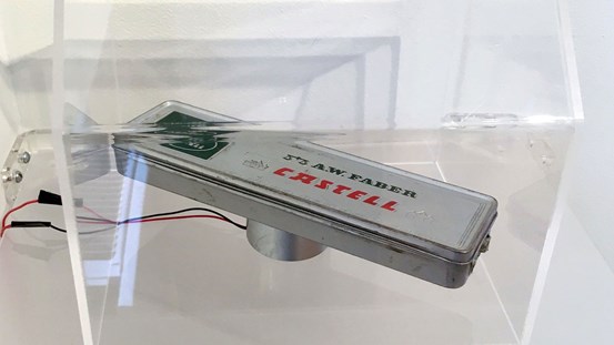 Ett plåtpennskrin av märket Faber Castell ligger i en kub av plexiglas med inbyggt ljud.