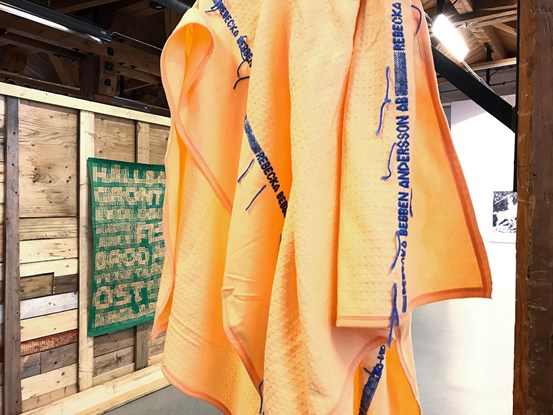 En hängande orange filt med text i blått broderat: Rebecka Bebben Andersson AB. 