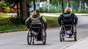 Två personer som tar sig fram med hjälp av rullstolar