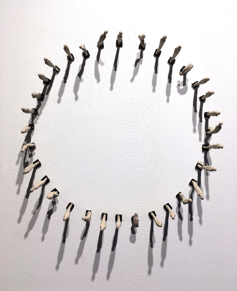 På väggen syns en ring bestående av små människor med kroppen i olika ställningar. De 32 figurerna kastar långa skuggor.