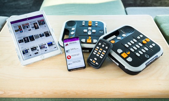 Surfplatta, mobiltelefon och taltidningsspelare med fjärrkontroller placerade på ett bord.
