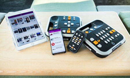 Surfplatta, mobiltelefon och taltidningsspelare med fjärrkontroller placerade på ett bord.