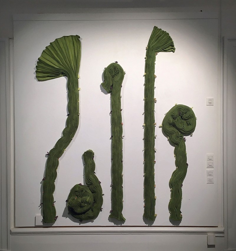 Ett grönt tvådimensionellt verk hängande på en vägg, i plisserad och färgad filt. Det tjocka tyget, stänkt med små färgade bitar som sytts på med jämna mellanrum, har formats till höga strängar med mer eller mindre ihoprullade avslut, som påminner om papyrus och kaktus, eller en kräkla. 