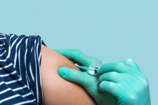 Bilden föreställer en persons arm som ges vaccination med en spruta.