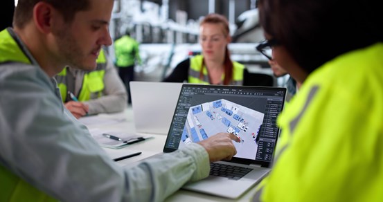 Personer sitter i en industrimiljö framför en datorskärm och utvecklar programvara.