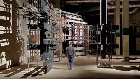 En går bortåt i bild, mellan stora träkonstruktioner. 