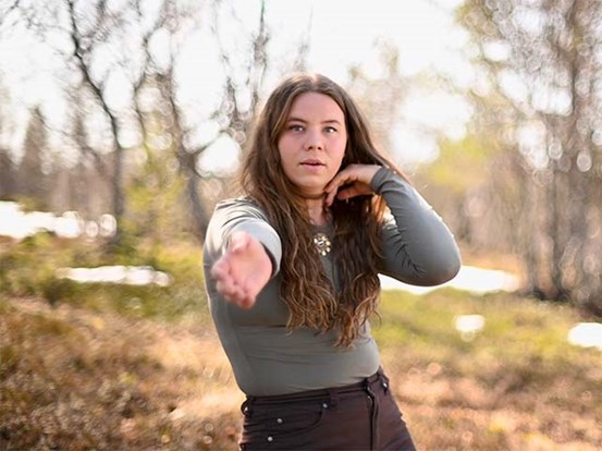 Konstnären Marika Renhuvud står ute i naturen och gör en danspose.