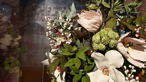 Foto av detalj av installation. Till höger en del av en stor blombukett, gjord i socker. Rosa och vita blommor med gröna blad. 