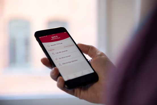 Hand som håller i telefon med skärmbild på 1177 appens startsida