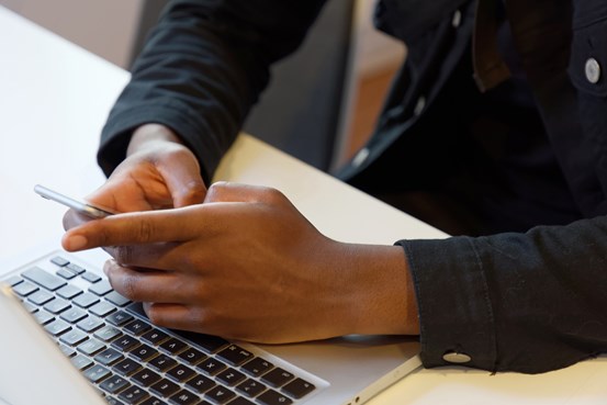 Händer som skriver på en smart telefon vid en laptop-dator.