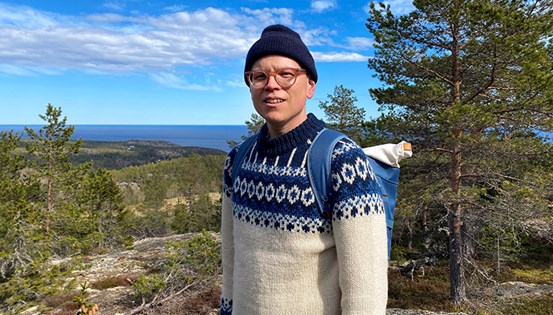 Porträttbild på Niklas Selin som står på ett berg i skogen
