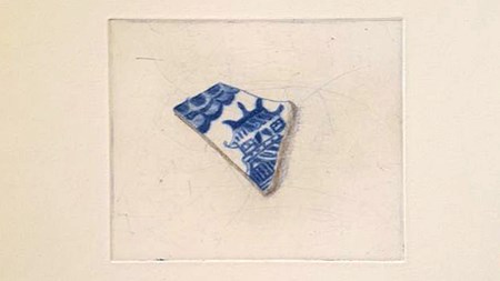 Grafiskt tryck. En porslinsskärva med ett blått mönster ligger på en vit yta. 