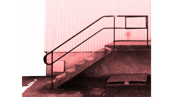 Monokromt foto i rosa ton. En betongtrappa med metallräcke sedd från sidan. En del av byggnadens fasad syns också.