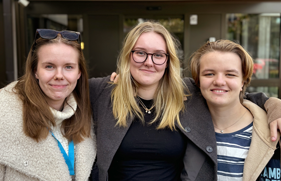 Tre unga tjejer, lärlingar på Folktandvården, står bredvid varandra utomhus.