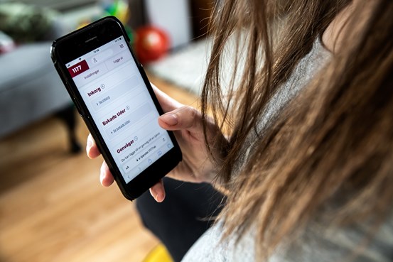 Kvinna som håller i mobil med inloggningssidan till e-tjänster på 1177.se