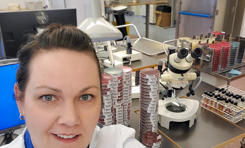  Porträttbild av en person i ett laboratorium med i bakgrunden ett mikroscoop