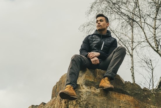 En ung man sitter på en klippa och blickar ut över landskapet