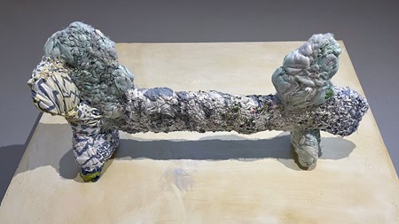 En skulptur i textilt material. Den är går i blå och vita toner, och påminner om en tax i formen.