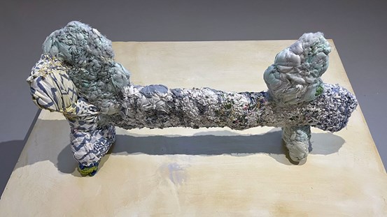 En skulptur i textilt material. Den är går i blå och vita toner, och påminner om en tax i formen.