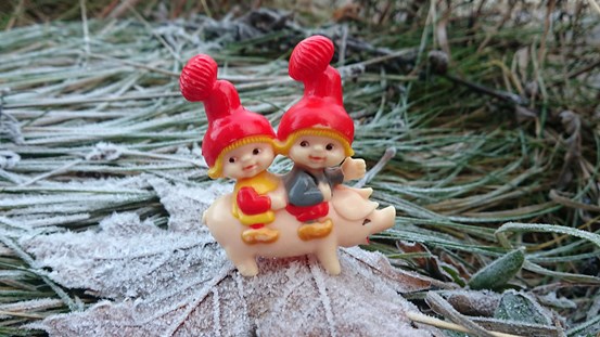 Foto utomhus av en leksak/pynt. Två tomtebarn rider på en gris på frostigt gräs. 