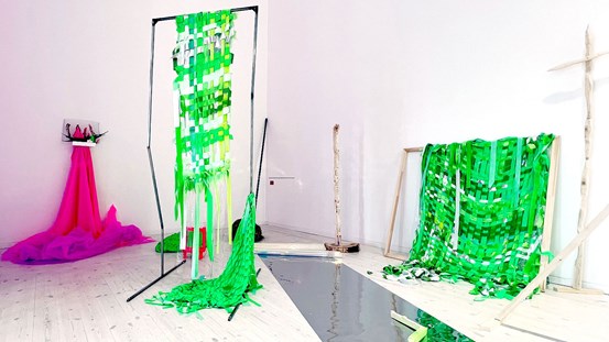 Längre in i rummet ligger sjok av gröna tygremsor, hopflätade med traditionell korgflätningsmetod. Här och var uppstår små fristående installationer. En vacker rosa tyllexplosion flödar ner från en hylla med abstrakta organiska former, skulpturala växtformer av tyg. 