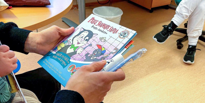 Vuxen visar bok om karies med Pelle Svanslös till ett barn. Hen håller också i en tandborste