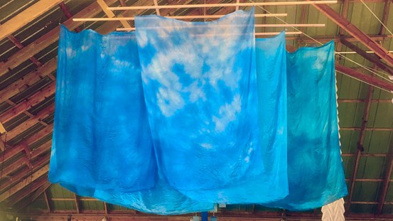 Flera stora sidentyger i som skiftar i blå nyanser hänger från trätaket. 
