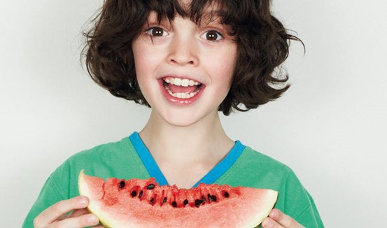 Glad pojke som håller i en bit vattenmelon.