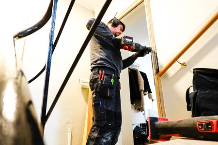En hantverkare som arbetar med ett handhållet verktyg vid en innervägg.
