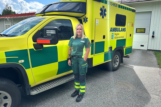 Ulrica Maistedt står i sina gröna och gula arbetskläder framför en av regionens ambulanser