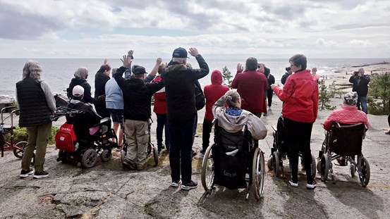 En grupp människor tittar ut över havet från en hög höjd, några sitter i rullstolar